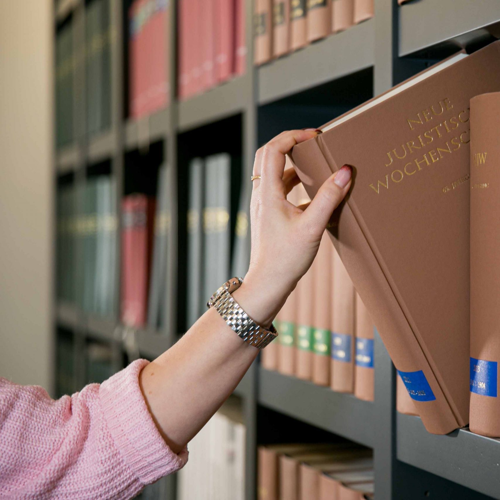 Eine Person nimmt ein Buch aus einem modernen Bücherregal.